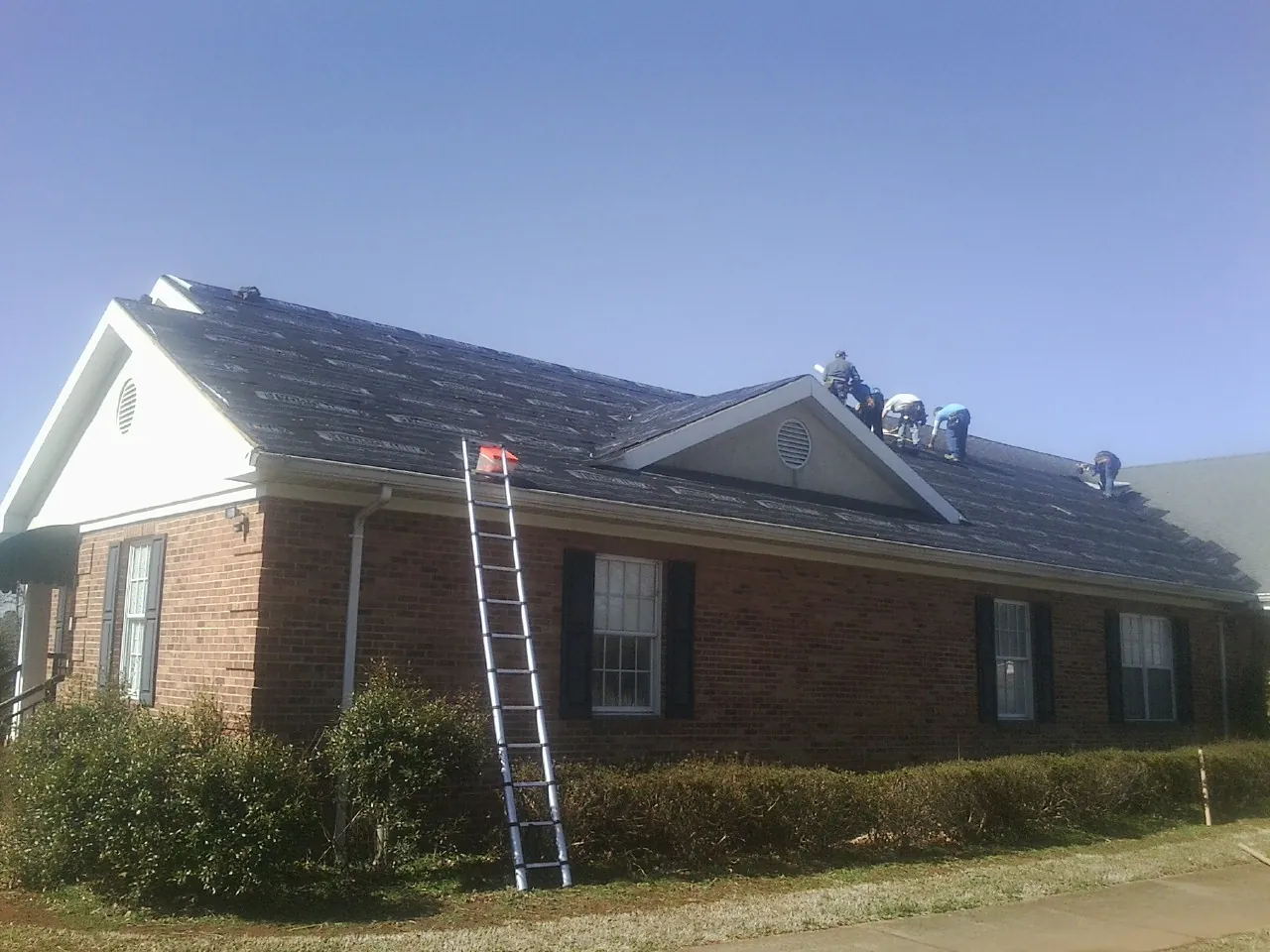 Crew tearing shingles off a brick ranch roof with a ladder set — Emergency Roof Repair work by our crew in Antelope