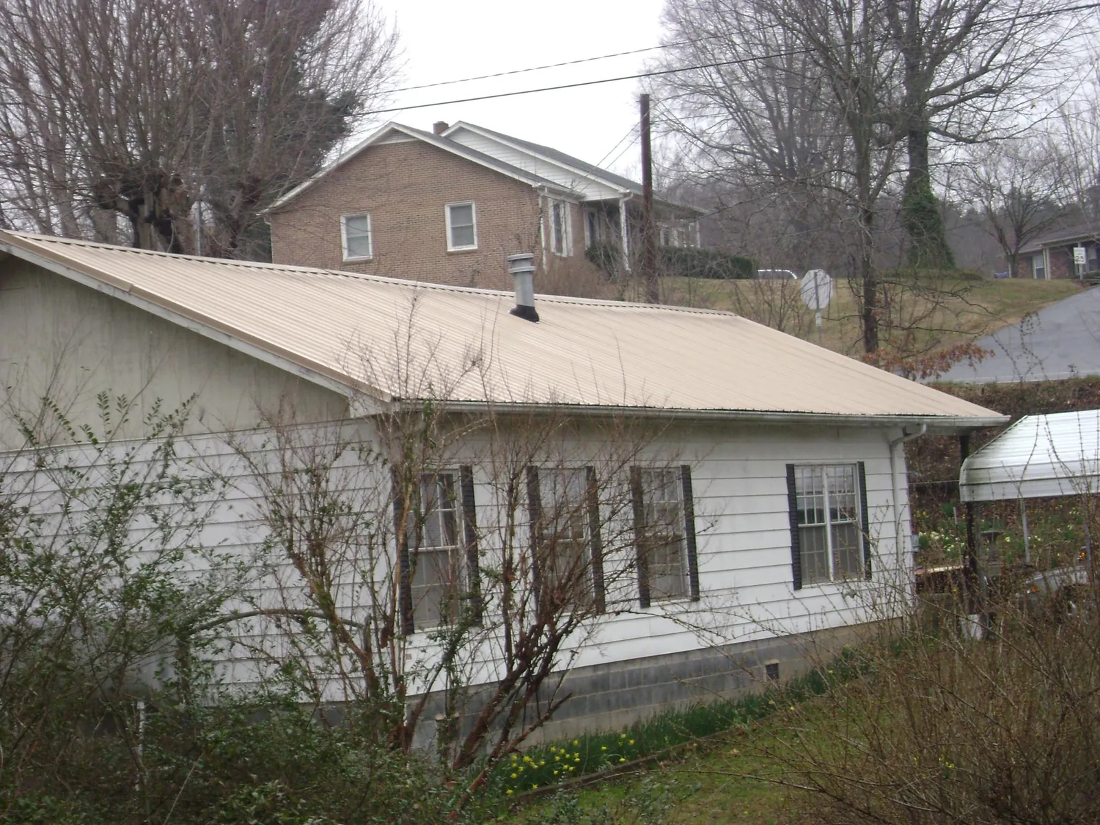 Tan metal roof on a white sided house set into a hillside — Commercial Roofing by Roofing Brothers in Antelope